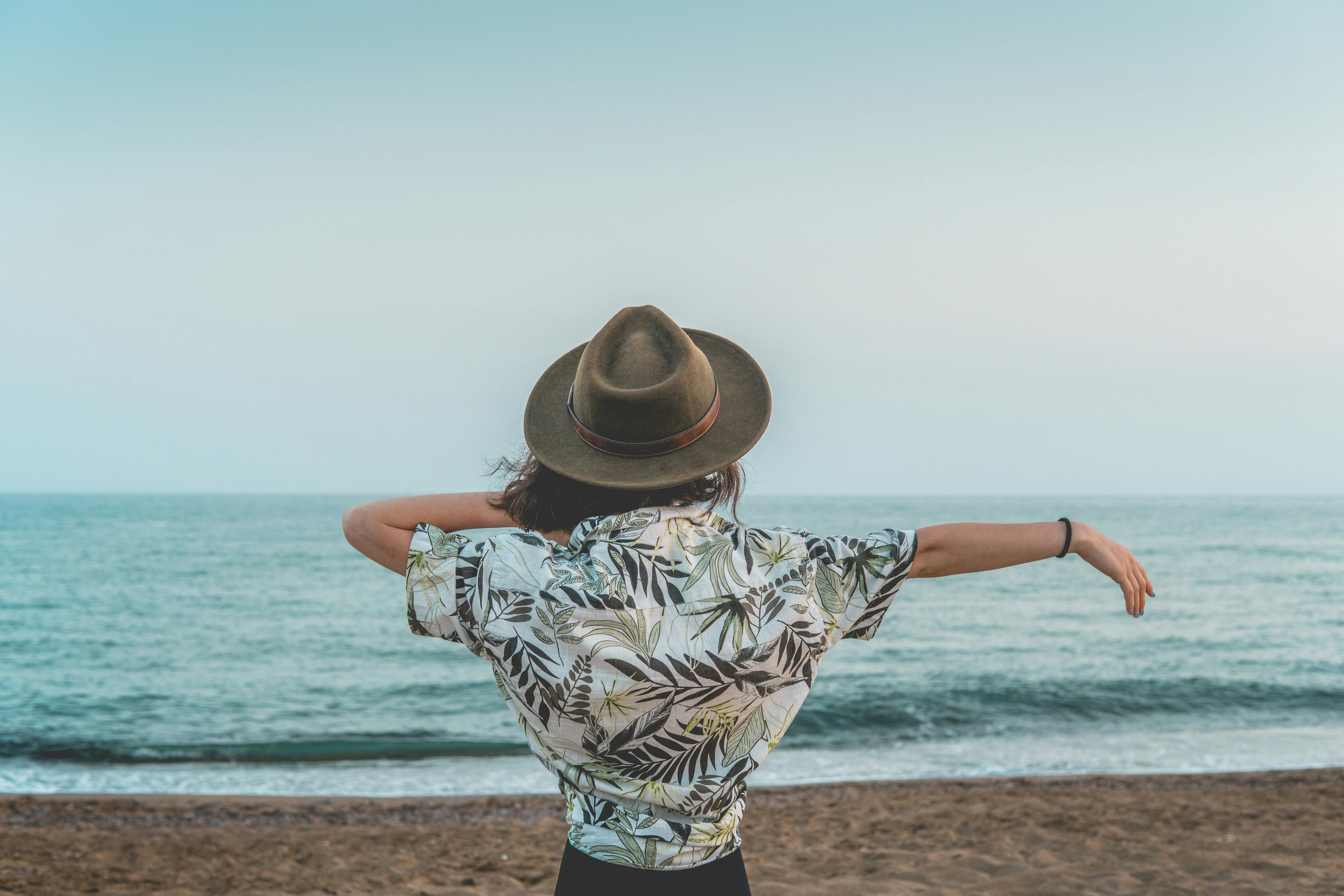 woman in white and black floral shirt and brown hat standing on beach during daytime